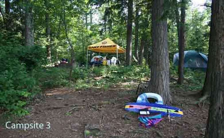 a tent in the woods with another tent area with just a yellow tarp roof